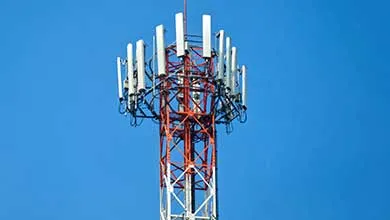 Red and white cell phone tower top with multiple antennas against a clear blue sky.